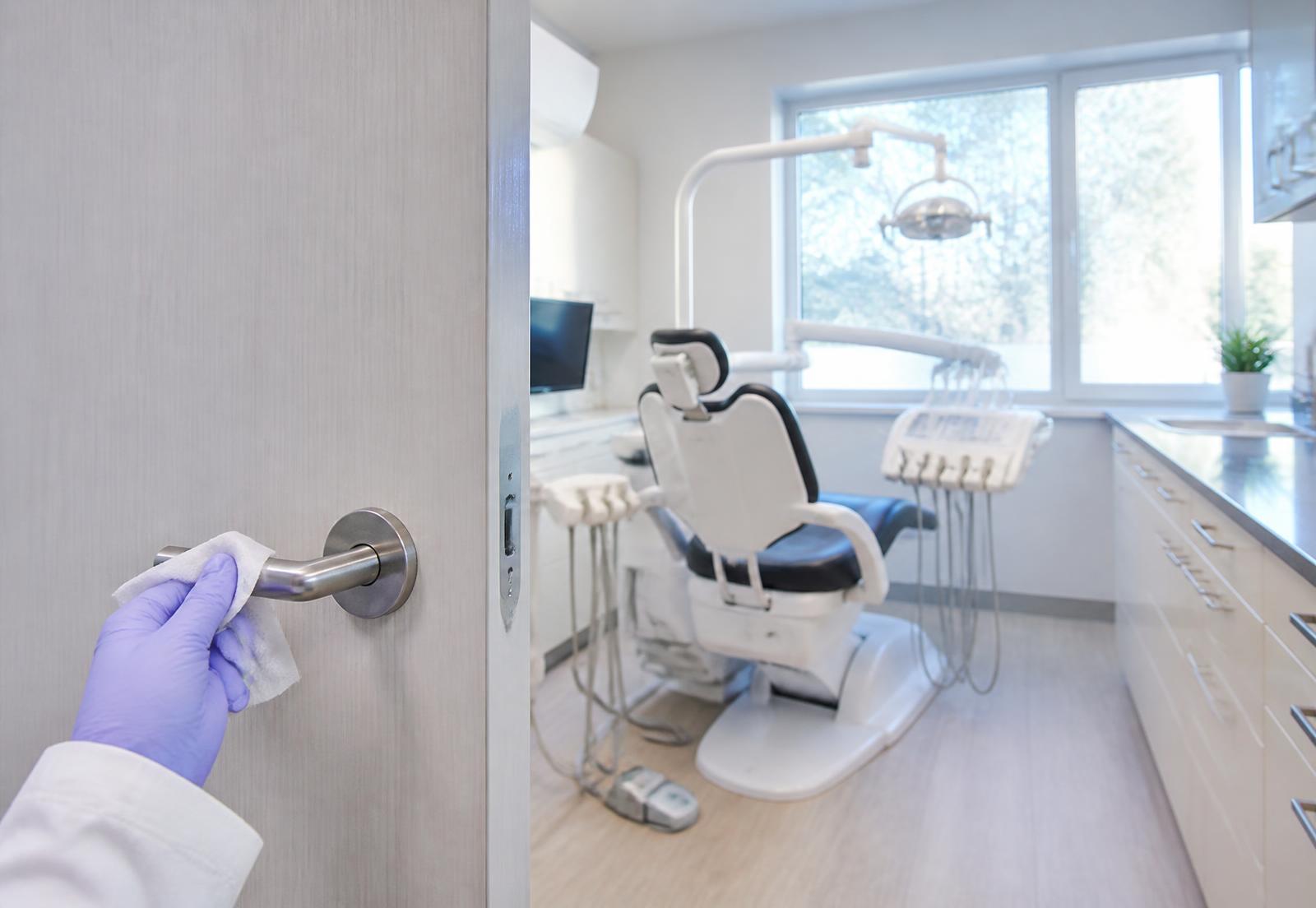 Gloved hand disinfecting a door handle in a clean dental office